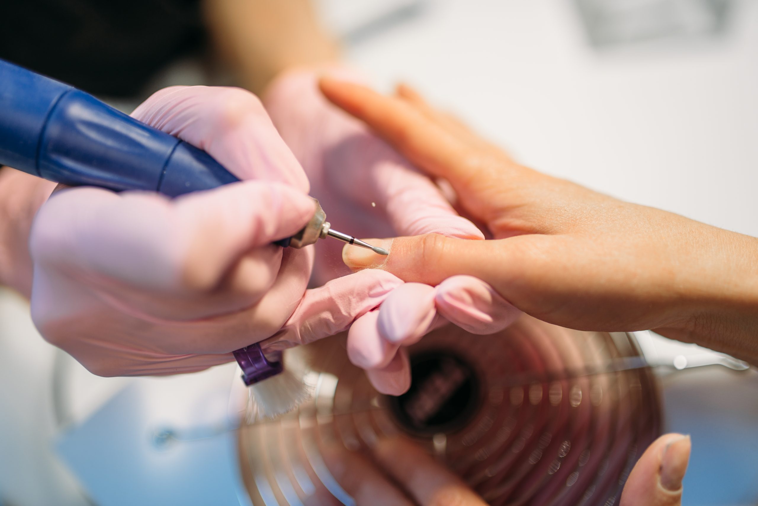 Beautician in gloves polishing nails of female client, top view, manicure in beauty salon. Manicurist doing hands care cosmetic procedure