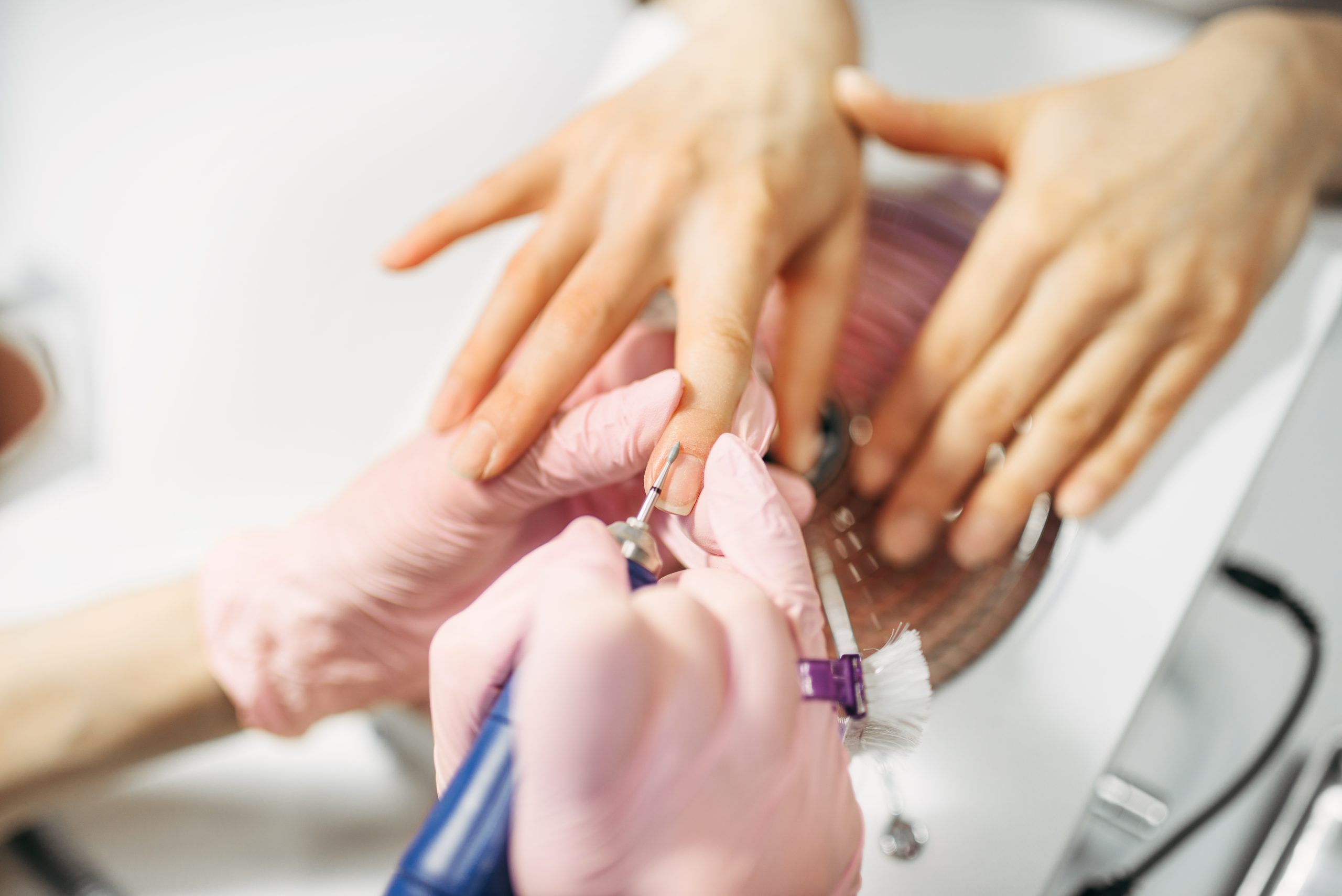 Beautician in gloves polishing nails of female client, top view, manicure in beauty salon. Manicurist doing hands care cosmetic procedure