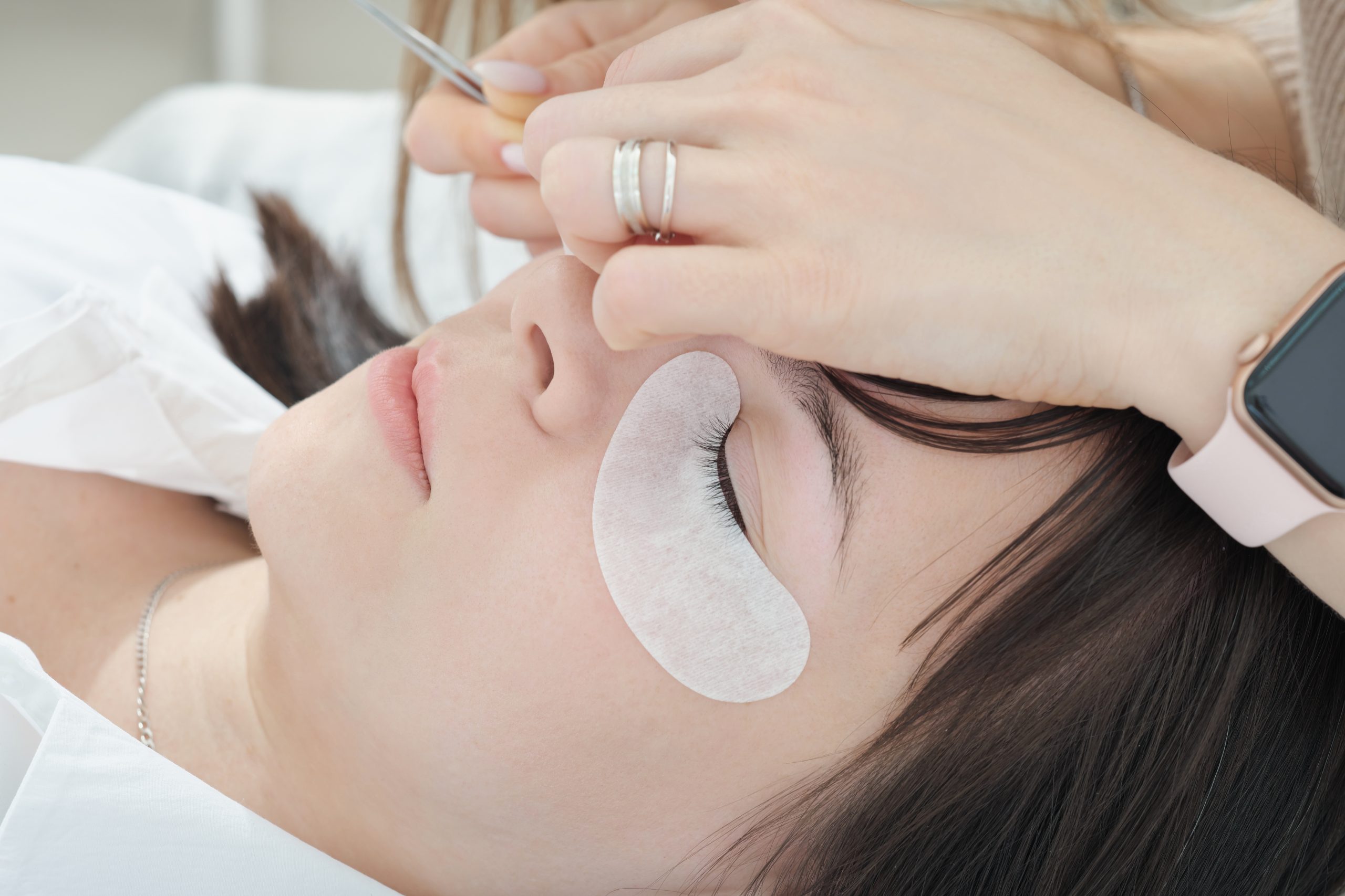 close up of caucasian woman client lying with eye closed during lash extension procedure. details of false lash making process