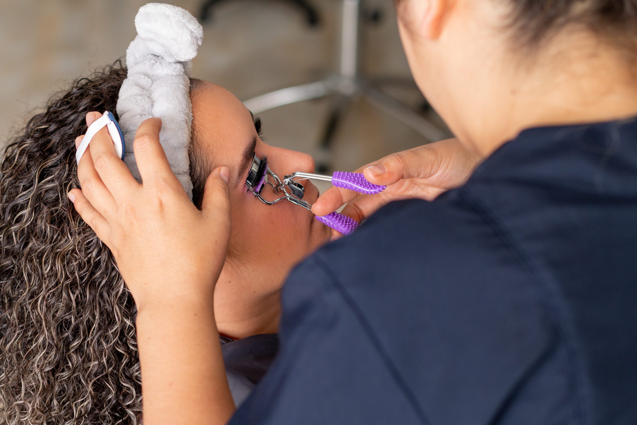 Professional makeup artist curling a woman's eyelashes with a curling iron.